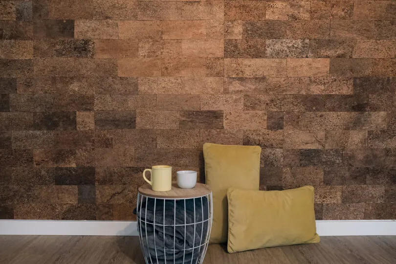 Wohnbereich mit Korkstruktur-Wandpaneel, rundem Tisch, Tasse, Schale und zwei Kissen auf dem Boden.