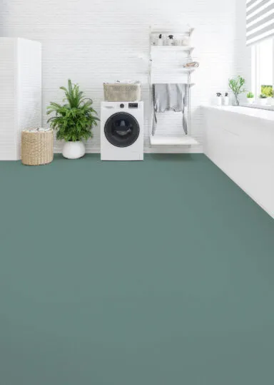 Moderne Waschküche mit grünem Linoleumboden, weißer Einrichtung, Waschmaschine, Regalen mit Körben und Pflanzen, Fenster mit gestreiften Jalousien.